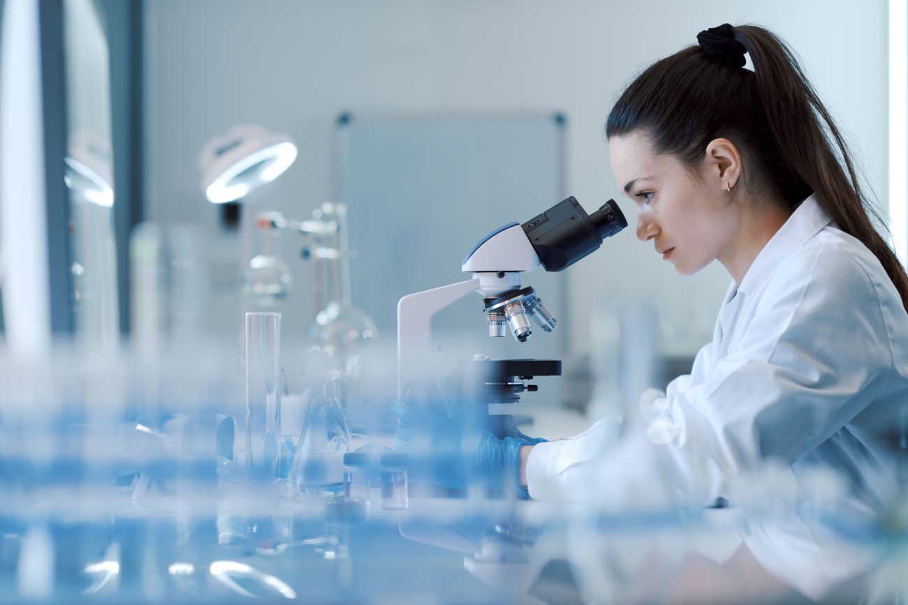Female researcher working in the lab, she is examining the samples under a microscope.