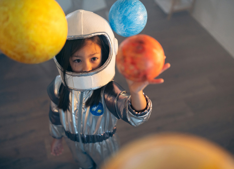 Girl in a space suit playing at home, exploring and learning about planets, imagining space travel.