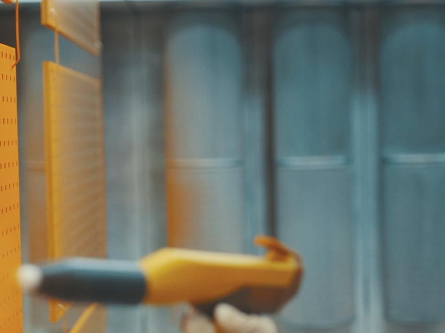 Man wearing protective gear with spray gun, painting metal panels orange using powder coating.