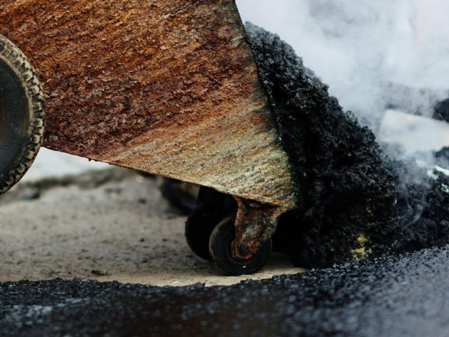 Road construction workers manually spread and adjust hot tar.